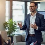 Rupert Freutsmiedl, erfahrener Coach und Unternehmensberater, spricht motiviert zu einem Team in einem modernen Büro.