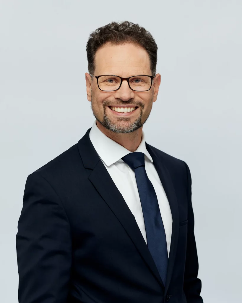 Sinnbild Coachings in Aachen mit Rupert Freusmiedl von dunkelweiss: Mann in Anzug mit Brille lächelt.