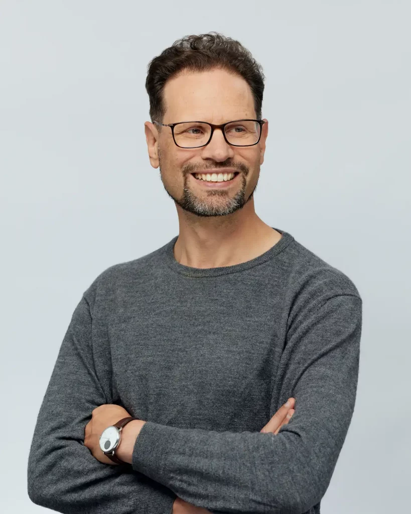 Sinnbild Kontakt aufnehmen mit Rupert Freusmiedl von dunkelweiss: Lächelnder Mann in grauem Pullover.