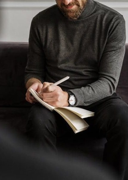 Sinnbild Karriere-Coachings in Aachen mit Rupert Freusmiedl von dunkelweiss: Mann in Anzug mit Brille lächelt.Mann schreibt in einem Notizbuch.